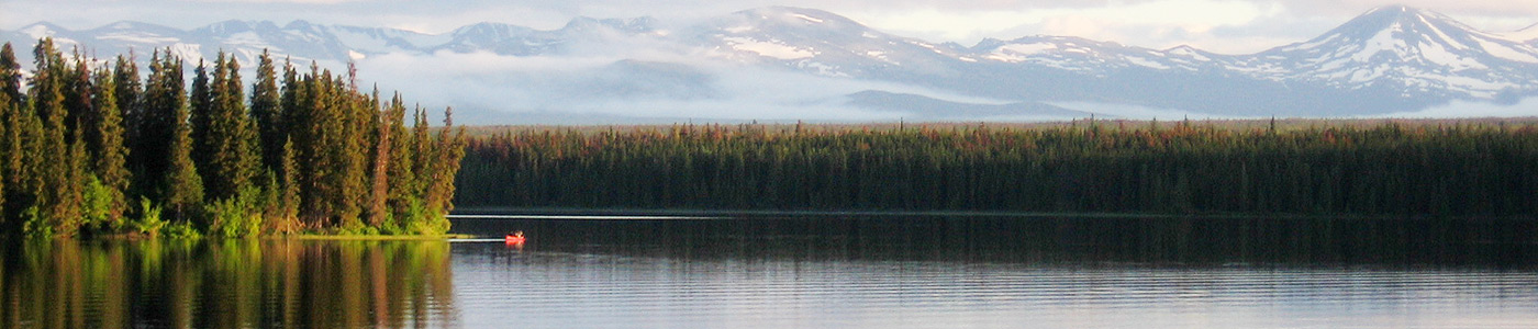 A red canoe near an island on the lake with mountains in the background.