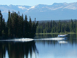 A floatplane takes off near the island with mountains behind.