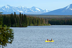 People paddle a yellow canoe across the water with mountains behind.