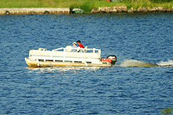 A couple drive a large pontoon boat across the water.