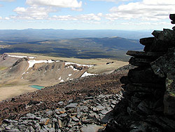 Photo courtesy of Miriam Schilling. A tiny green lake sits in a valley below a rocky peak with a cairn.