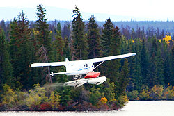 A blue and white plane takes off of Nimpo Lake with a canoe attached to the float.