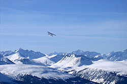 Photo property of resortsbc.com. A small plane flies over snowcovered peaks and valleys in winter.