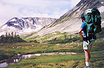 A hiker with packsack looks out over a long alpine valley.