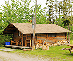 An older log cabin with deck and wood along wall.